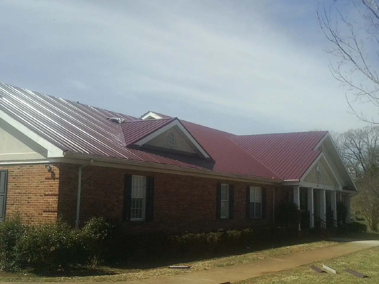 Red metal roof with gabled entries on a long brick building, from a Hail Damage Roof Repair job in North Adams