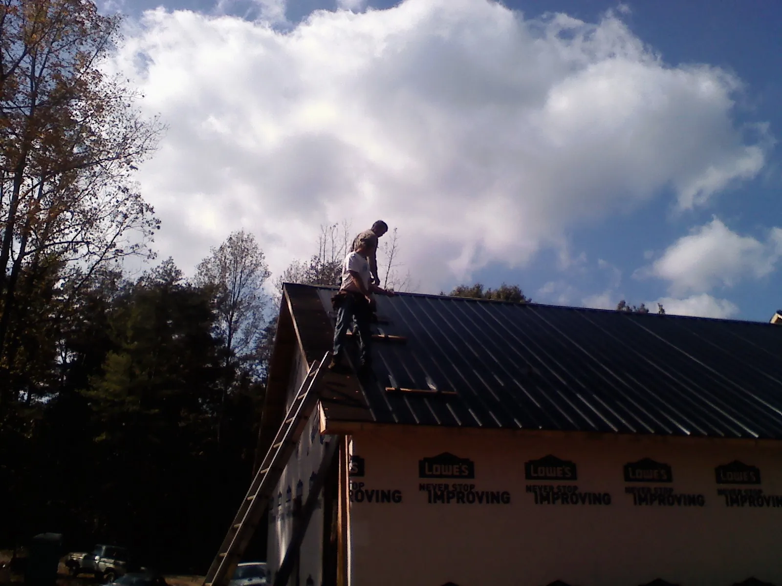 Roofer fastening dark metal panels high against a cloudy sky, from a Roof Inspection job in North Adams